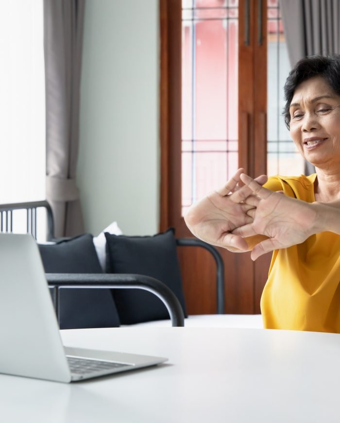 Older woman practicing chair yoga in front of a laptop